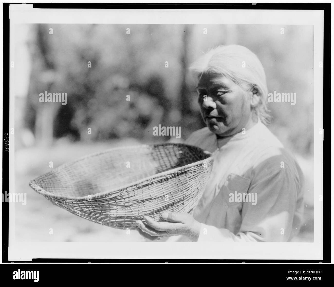 Sifting basket southern Miwok, Edward S. Curtis Collection., Curtis no. 3995., Published in: The North American Indian / Edward S. Curtis. [Seattle, Wash.] : Edward S. Curtis, 1907-30, v. 14, p. 100.. Indians of North America, Arts & crafts, California, 1920-1930. , Miwok Indians, Women, 1920-1930. , Baskets, 1920-1930. Stock Photo