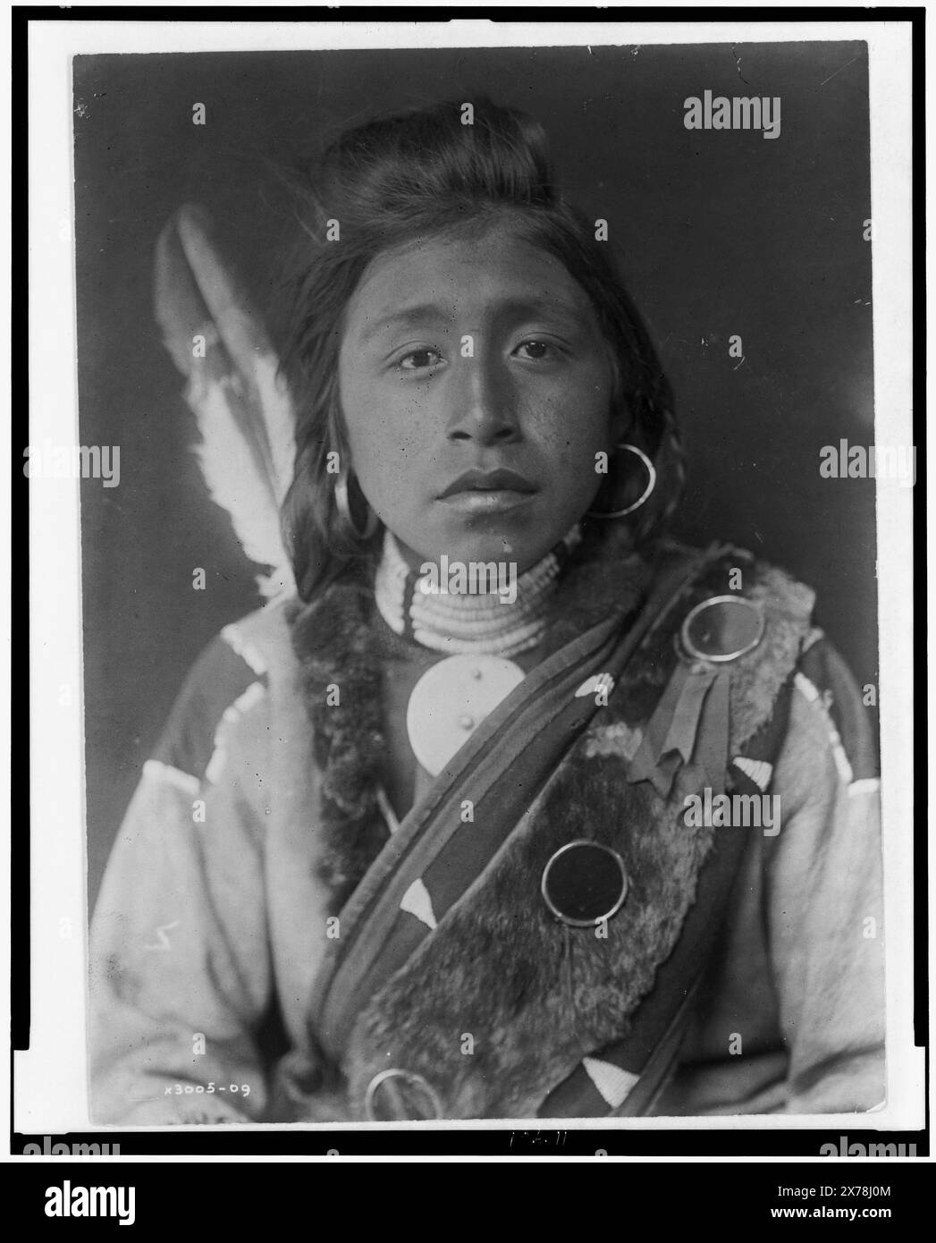 Kashhila Wishham. Male Chinookan Indian, head-and-shoulders portrait, facing front, with pompadour, fur wrapped braids, bead choker around neck, beaded buckskin shirt, fur sash over left shoulder, Edward S. Curtis Collection., Curtis no. 3005-09., Published in: The North American Indian / Edward S. Curtis. [Seattle, Wash.] : Edward S. Curtis, 1907-30, suppl., v. 8, pl. 283.. Kashhila-Wisham. , Indians of North America, Clothing & dress, 1910. , Chinookan Indians, Clothing & dress, 1910. Stock Photo
