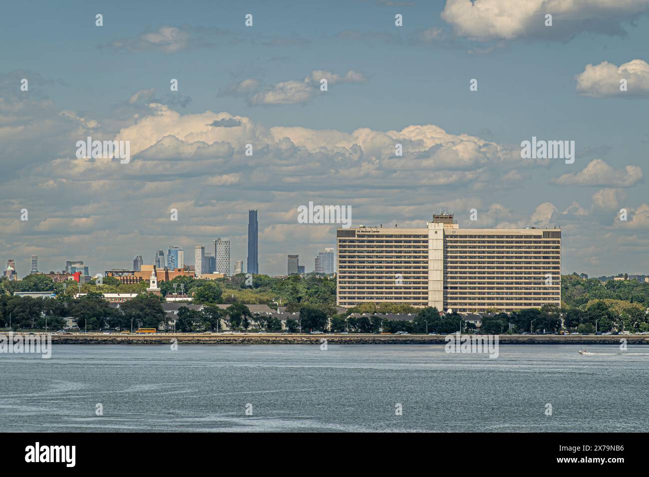 New York, NY, USA - August 1, 2023: Brooklyn VA Medical Center Bldg and Brooklyn skyline. Green trees on coastline under blue cloudscape Stock Photo