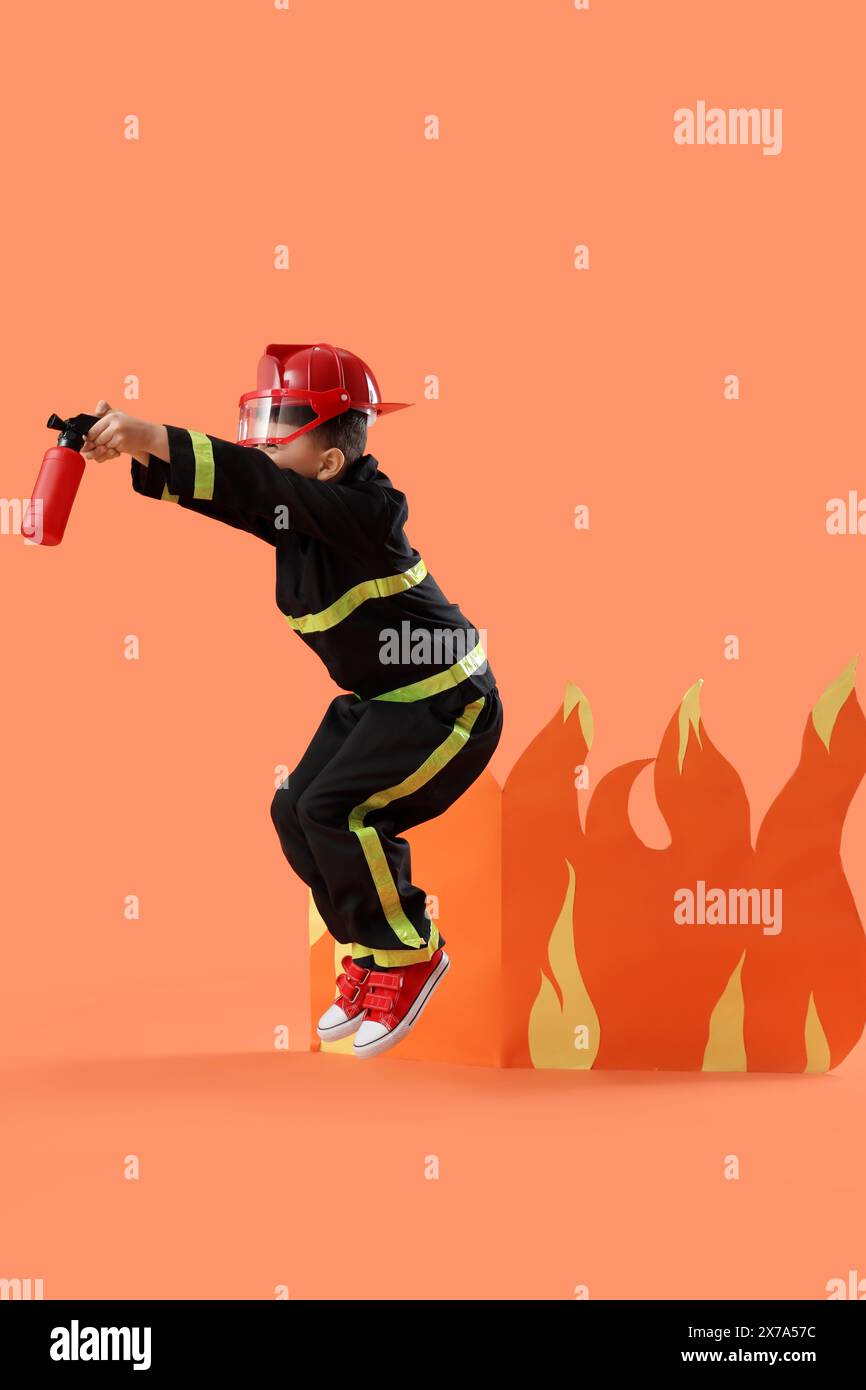 Cute little firefighter with toy extinguisher and paper flame jumping ...