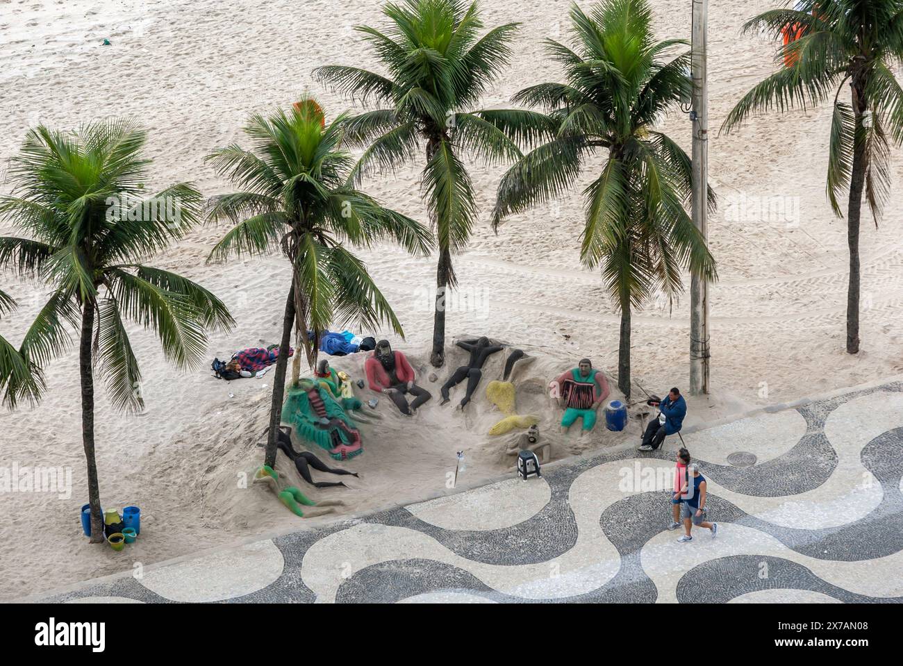 People walk past sand sculptures made on Copacabana Beach adjacent to ...