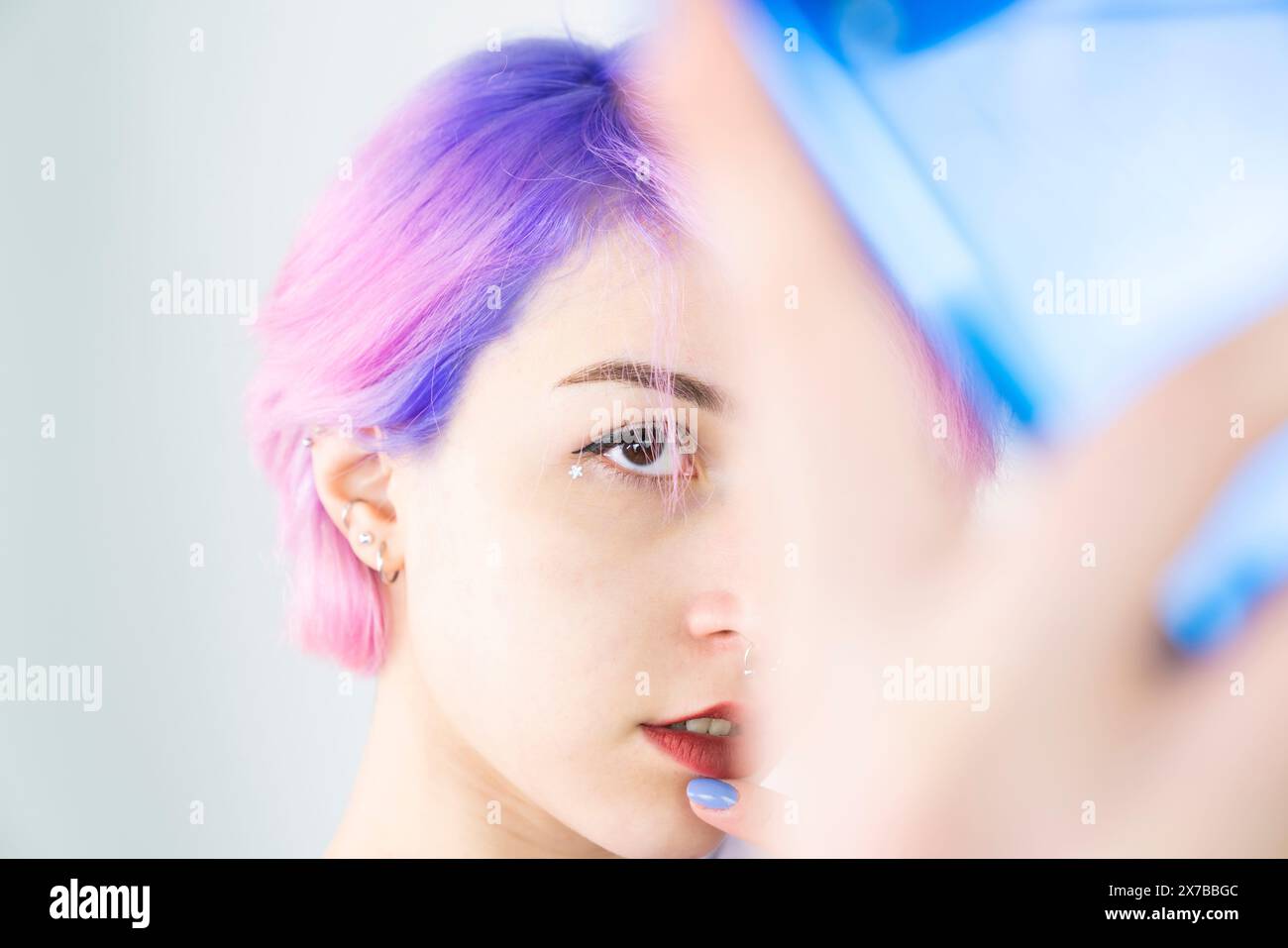 A young woman with blue and pink hair is taking a selfie with her cell phone. Generation z woman taking selfie on white background Stock Photo