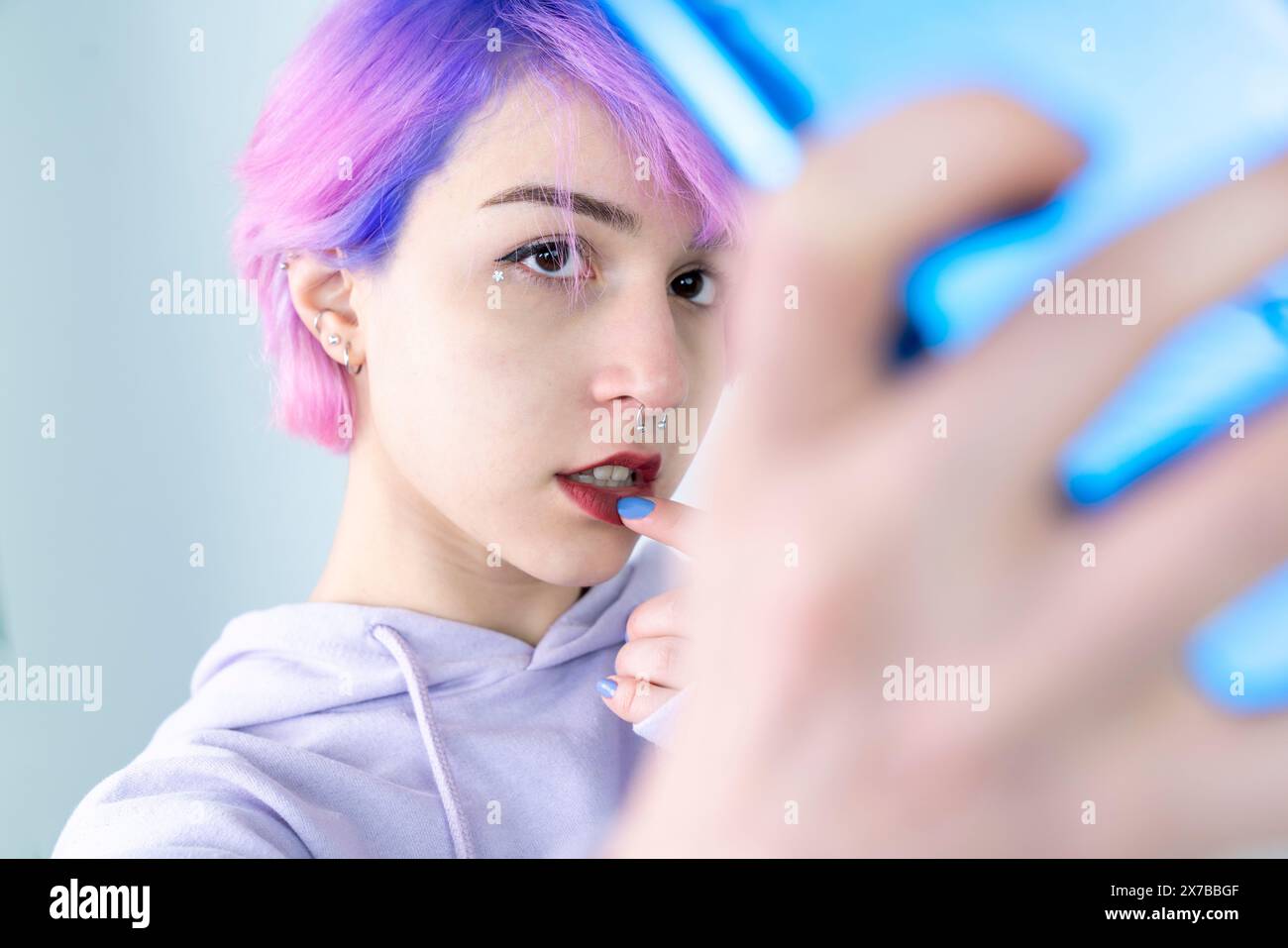 A young woman with blue and pink hair is taking a selfie with her cell phone. Generation z woman taking selfie on white background Stock Photo