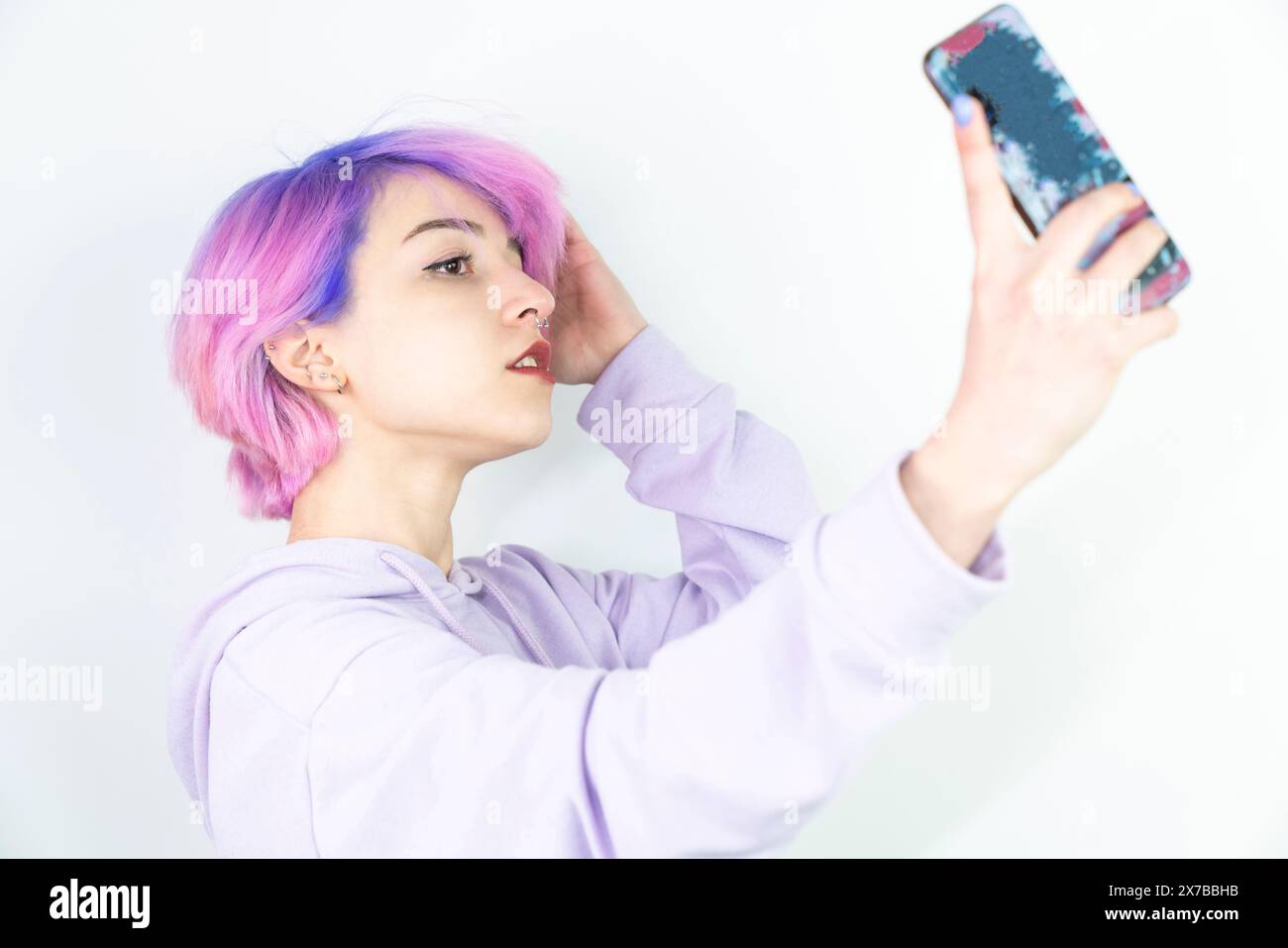 A young woman with blue and pink hair is taking a selfie with her cell phone. Generation z woman taking selfie on white background Stock Photo