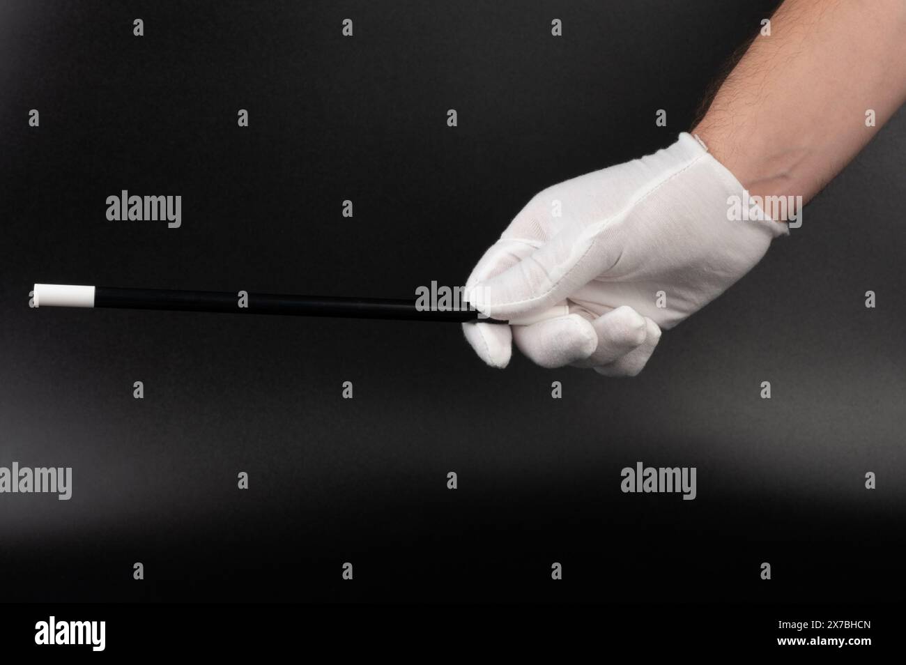 Hand in white glove hold magic wand isolated on black studio background Stock Photo