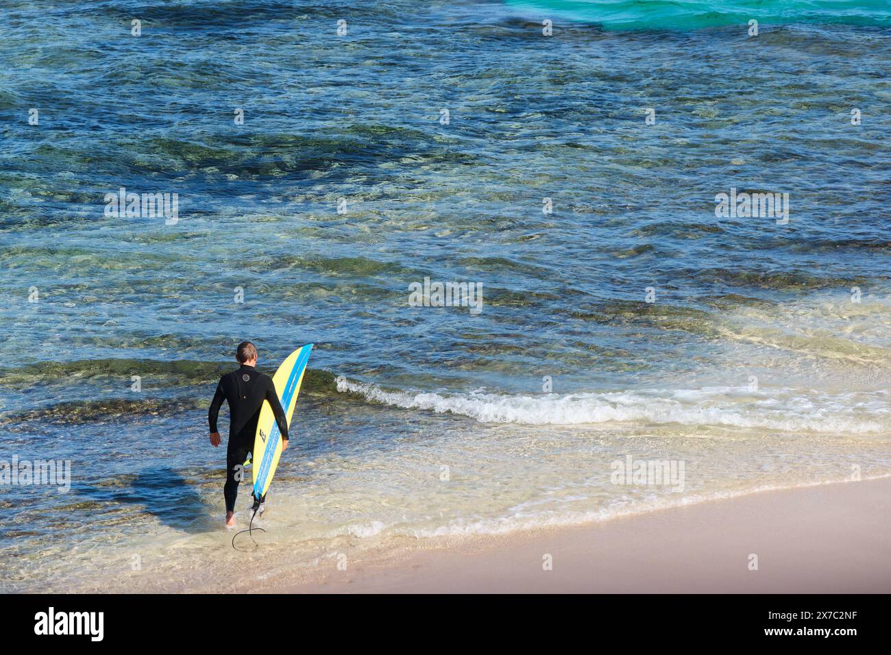 A surfer wearing a wetsuit carrying a surfboard heads into the ocean at