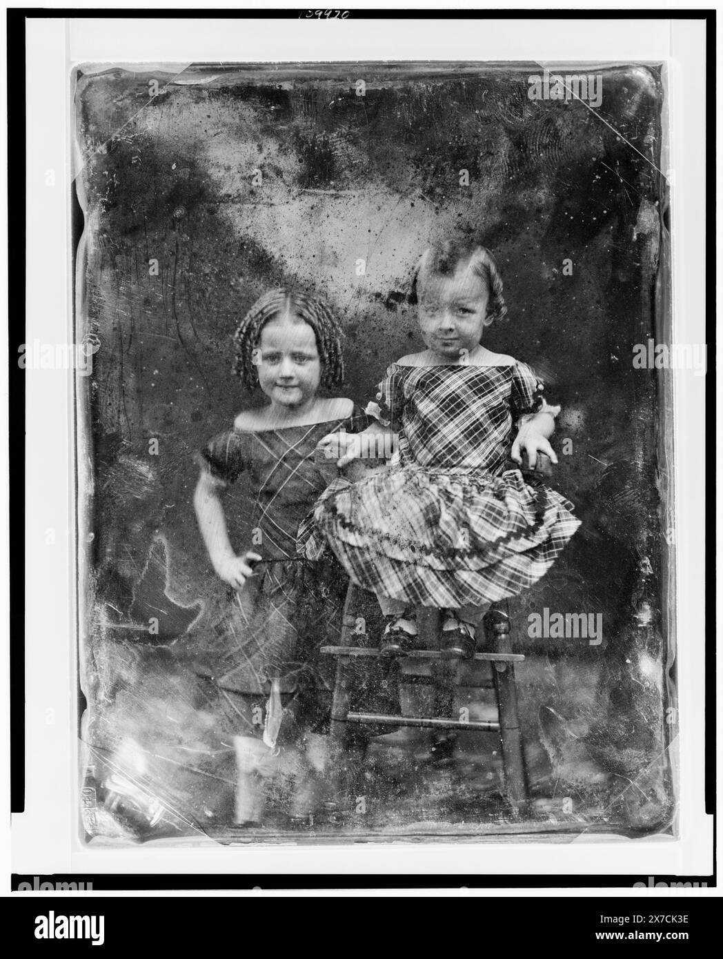 Two unidentified girls, about three and five years of age, the younger child seated in high chair, older one standing beside her on left, both nearly facing front, Scratched on back of plate: 98., Hallmark: [paschal lamb] 40 [Upside down A], Transfer; U.S. War College; 1920; (DLC/PP-1920:46153)., Forms part of: Daguerreotype collection ,  Produced by Mathew Brady's studio. Stock Photo