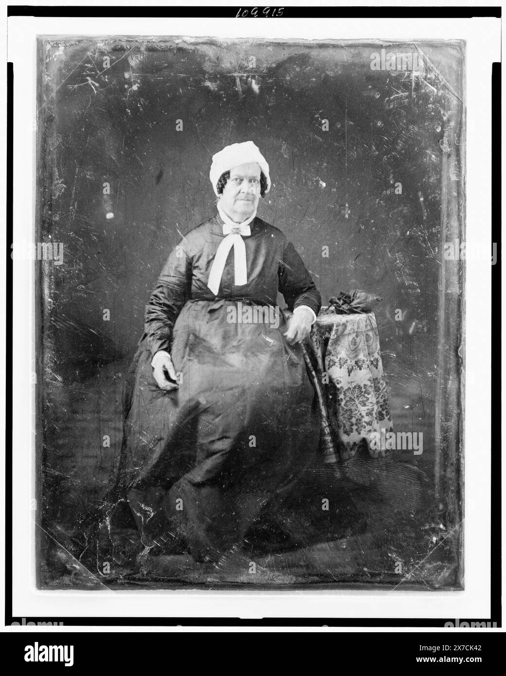 Unidentified woman, about 60 years of age, full-length portrait, facing front, seated beside small table with tablecloth and handbag, wearing white cap, Scratched on face of plate: 178. Scratched on back of plate: 80; 90., Transfer; U.S. War College; 1920; (DLC/PP-1920:46153)., Forms part of: Daguerreotype collection ,  Produced by Mathew Brady's studio. Stock Photo