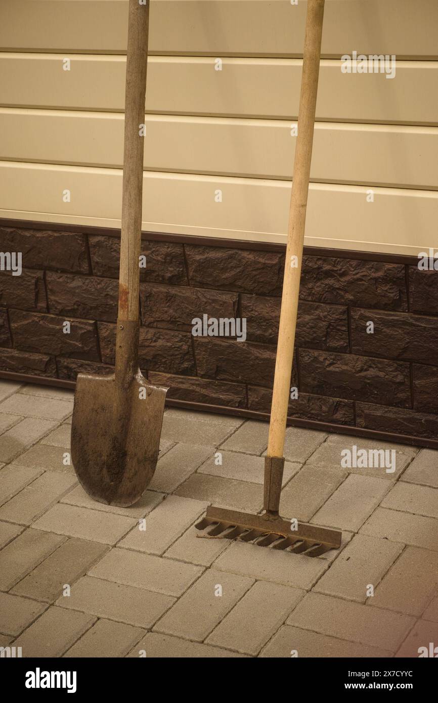 A shovel and a rake standing near wall of the house. Stock Photo