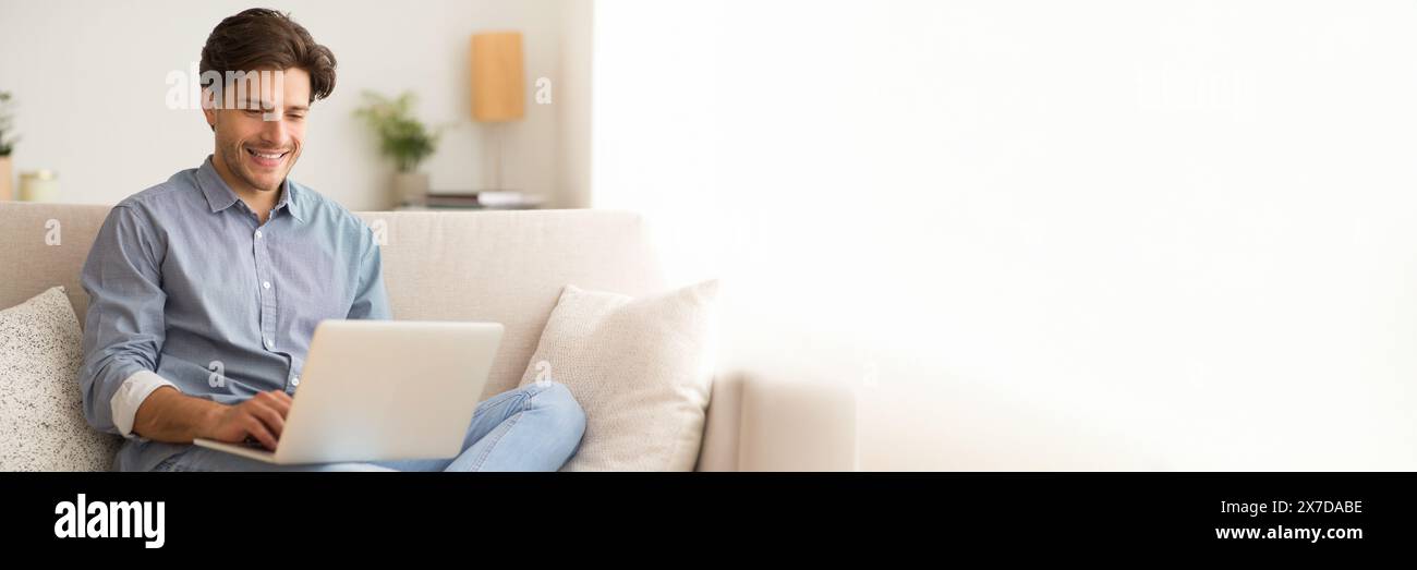 Happy young man sitting on couch, using laptop Stock Photo