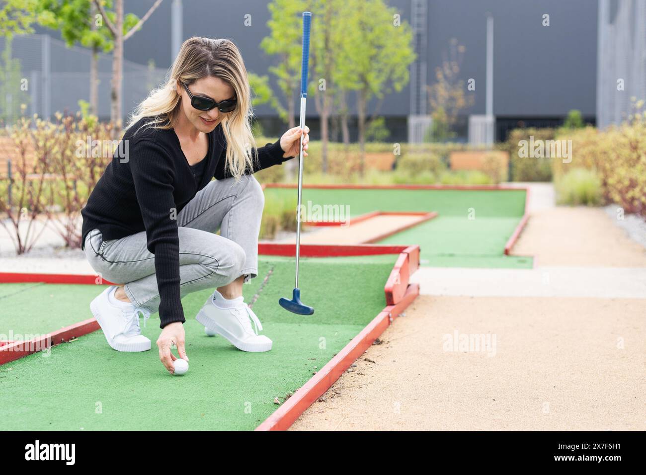 Woman playing mini golf and trying putting ball into hole. Summer ...