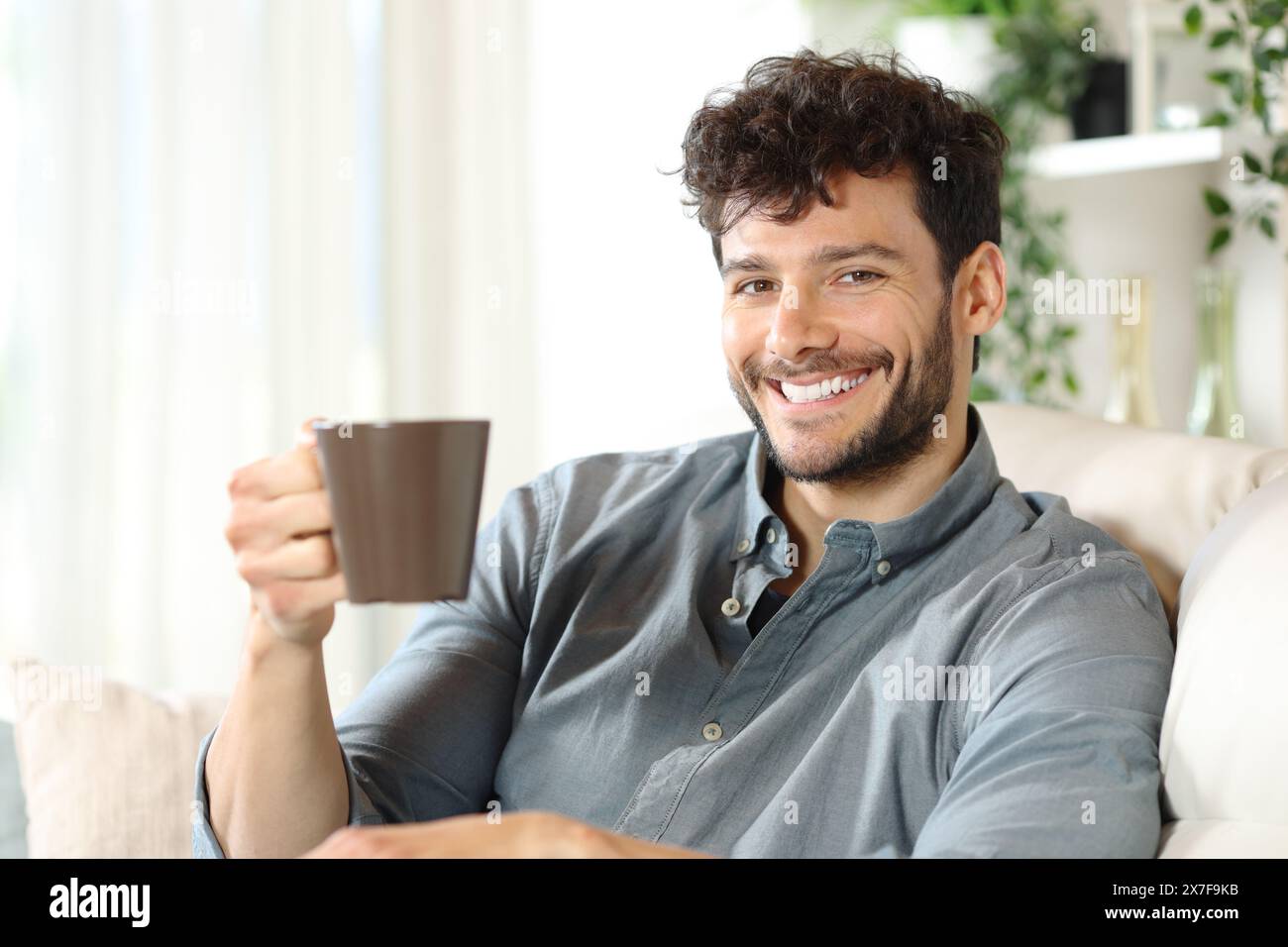 Happy man drinking coffee sitting on a couch at home looking at camera Stock Photo