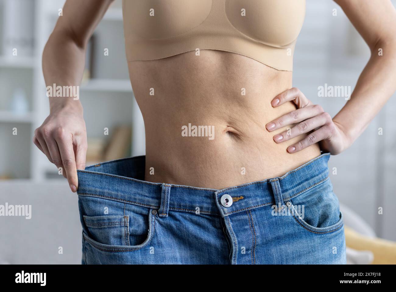 Close-up photo of female body part, thin waist, wearing wide jeans and showing result of weight loss, sport and diet. Stock Photo
