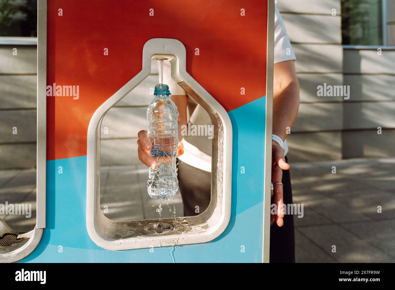 A woman pours drinking water into a water bottle in the city at a gas ...