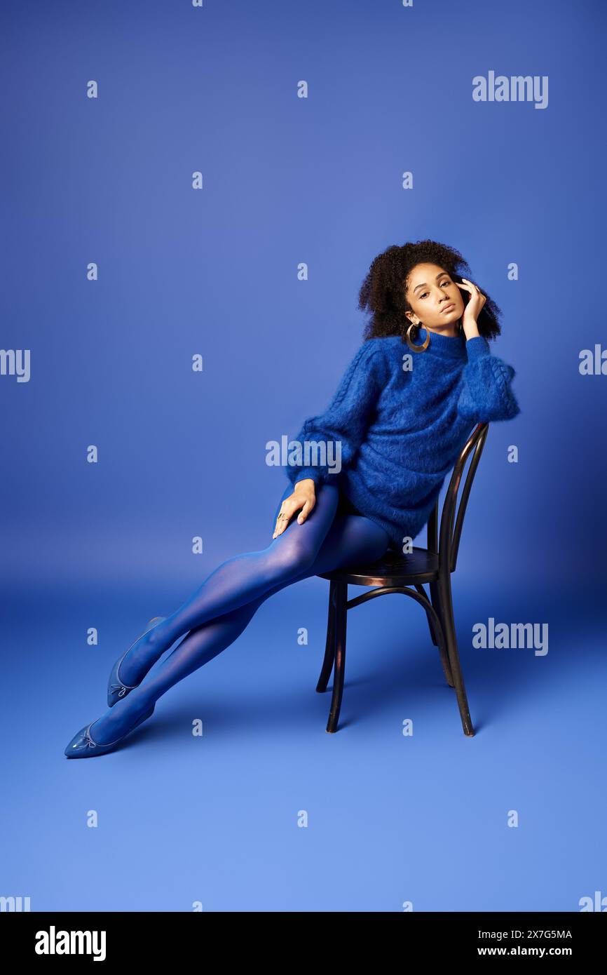 A young woman in a stylish blue dress sits elegantly on a chair against ...