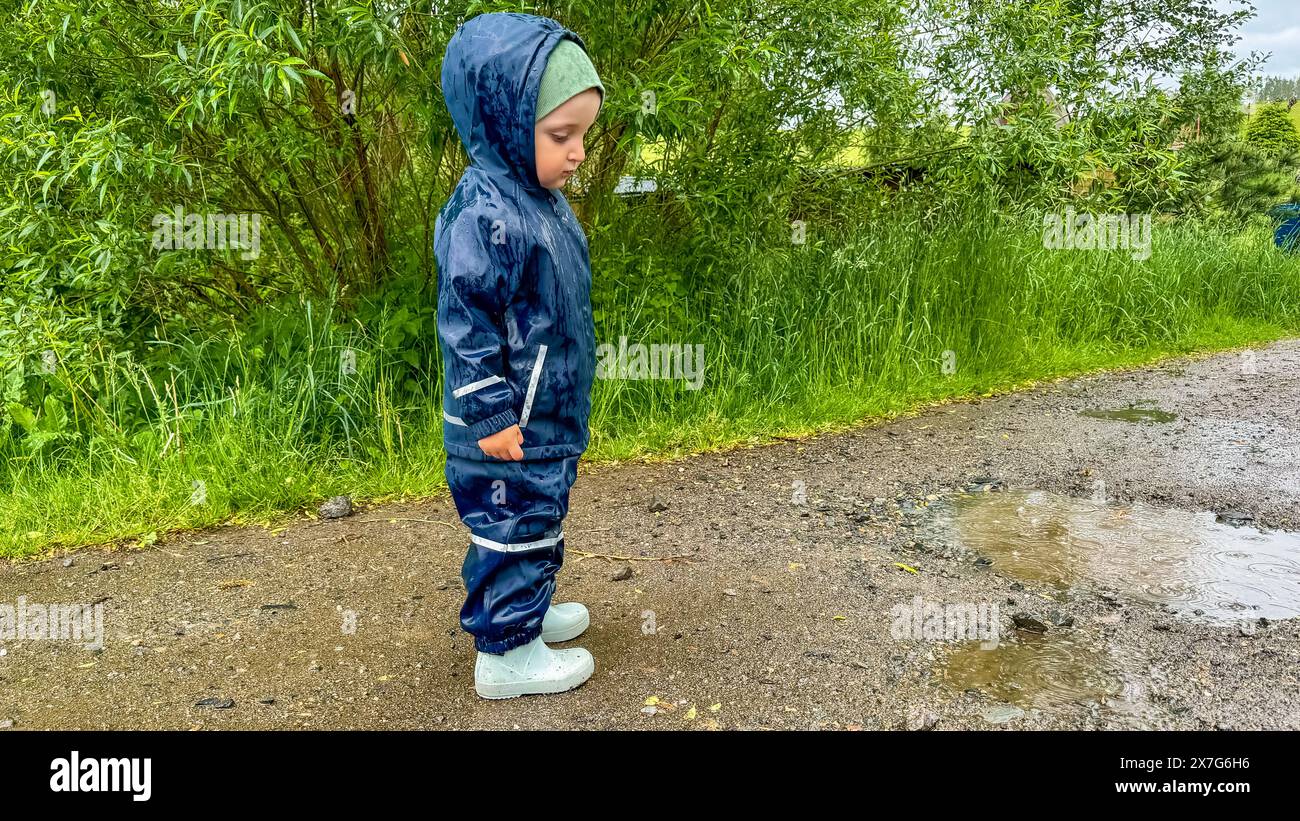 The child runs through puddles in rubber boots and a waterproof suit ...