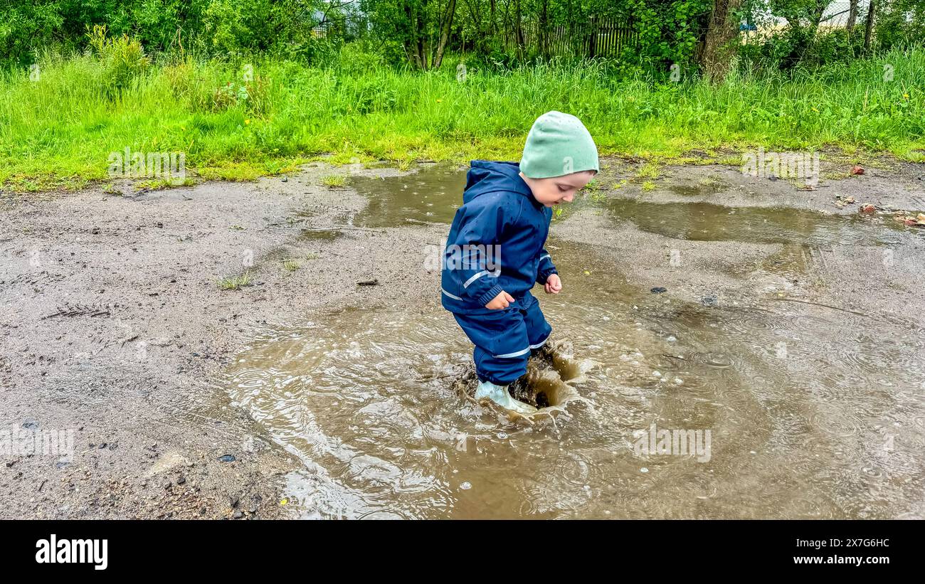 The child runs through puddles in rubber boots and a waterproof suit ...
