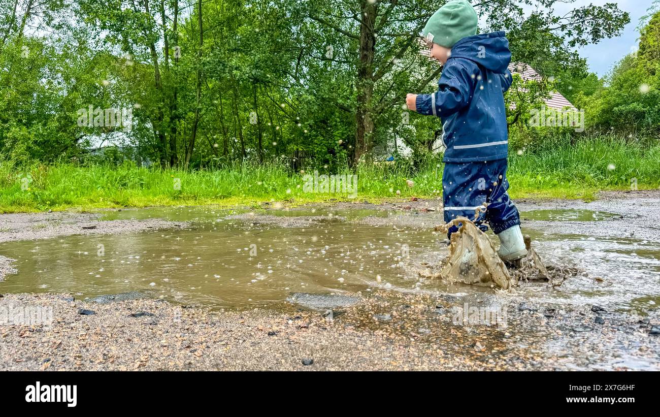 The child runs through puddles in rubber boots and a waterproof suit ...