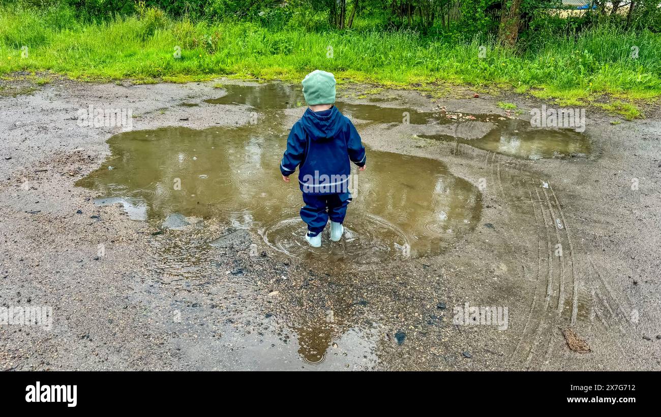 The child runs through puddles in rubber boots and a waterproof suit ...