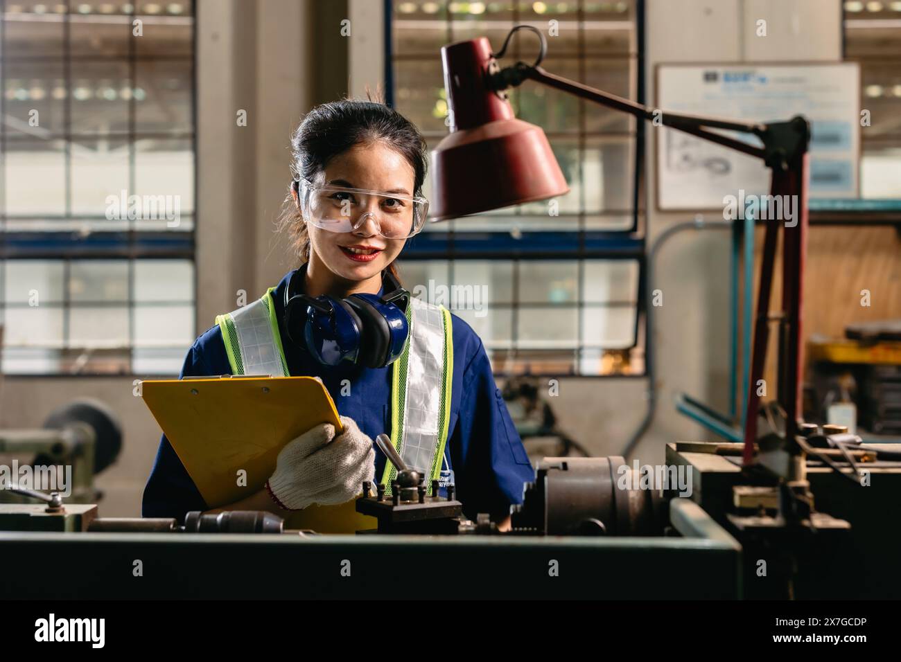 Portrait happy engineer worker with safety eyes protection glasses professional working with metal lathe milling machine heavy industry factory. Stock Photo