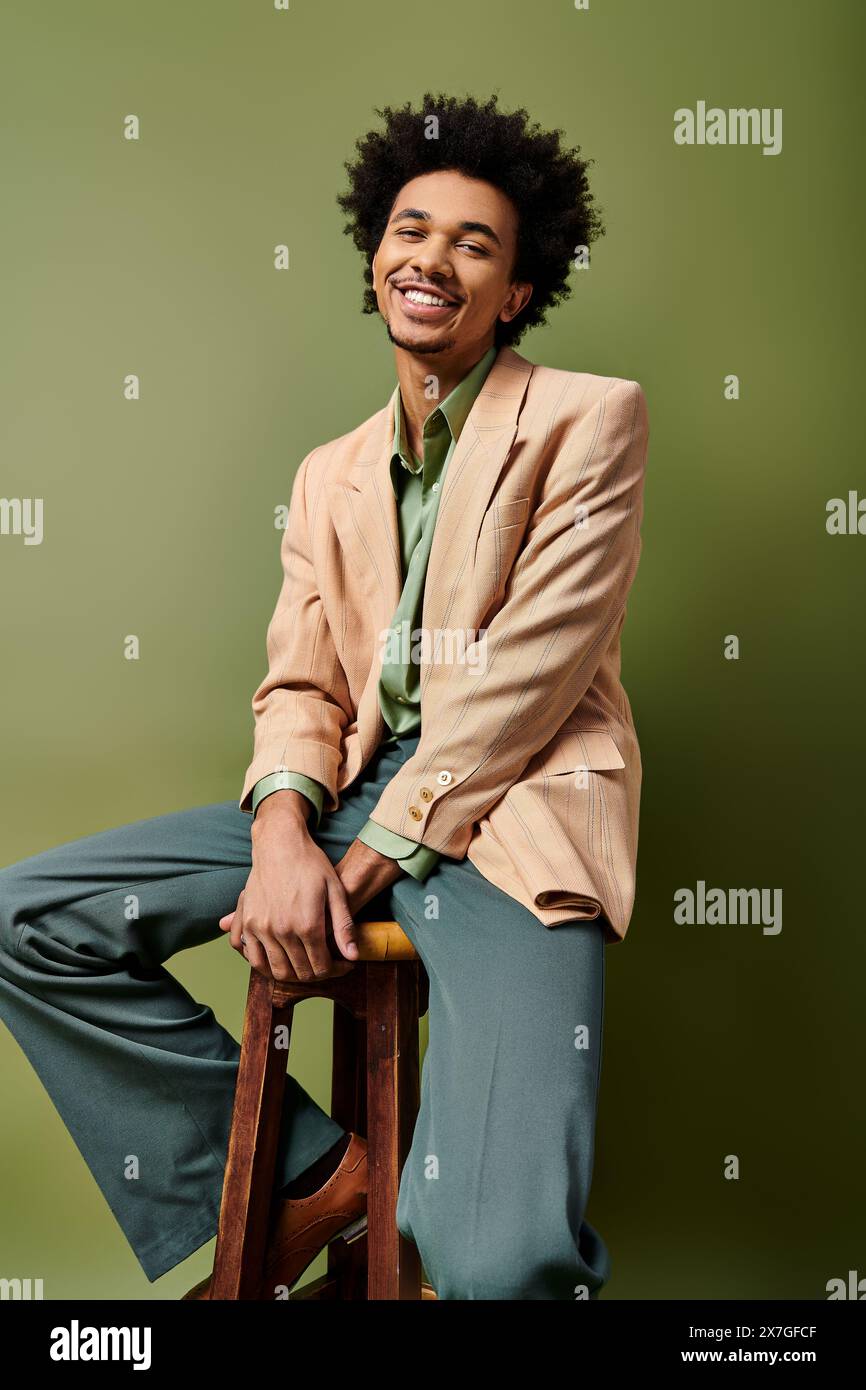 A stylish young African American man with curly hair sits atop a wooden ...