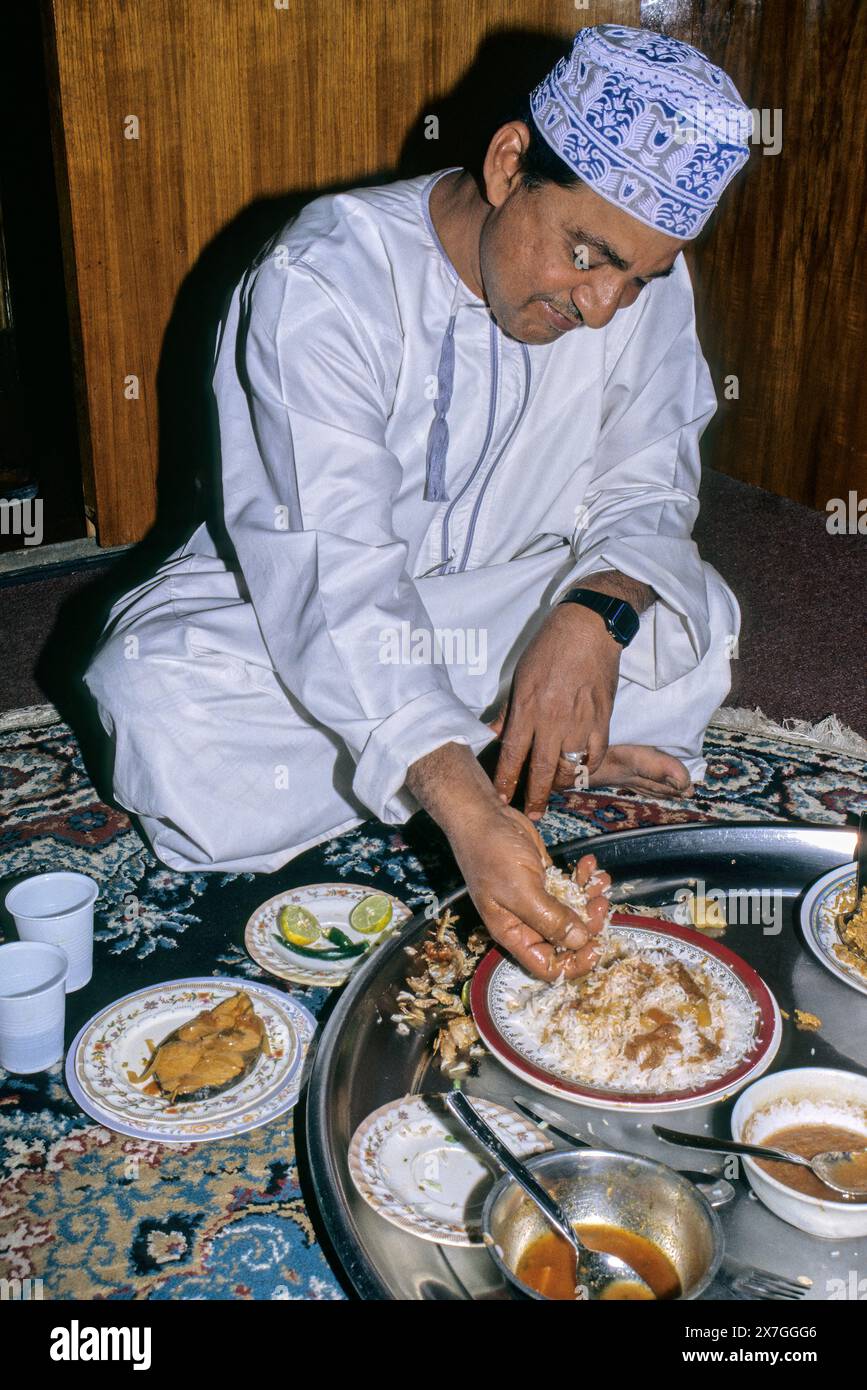 Nizwa, Oman, Arabian Peninsula, Middle East - Omani Man Eating Lunch of Fish, White Rice, and Sauce.  Meals are frequently eaten while sitting on the Stock Photo
