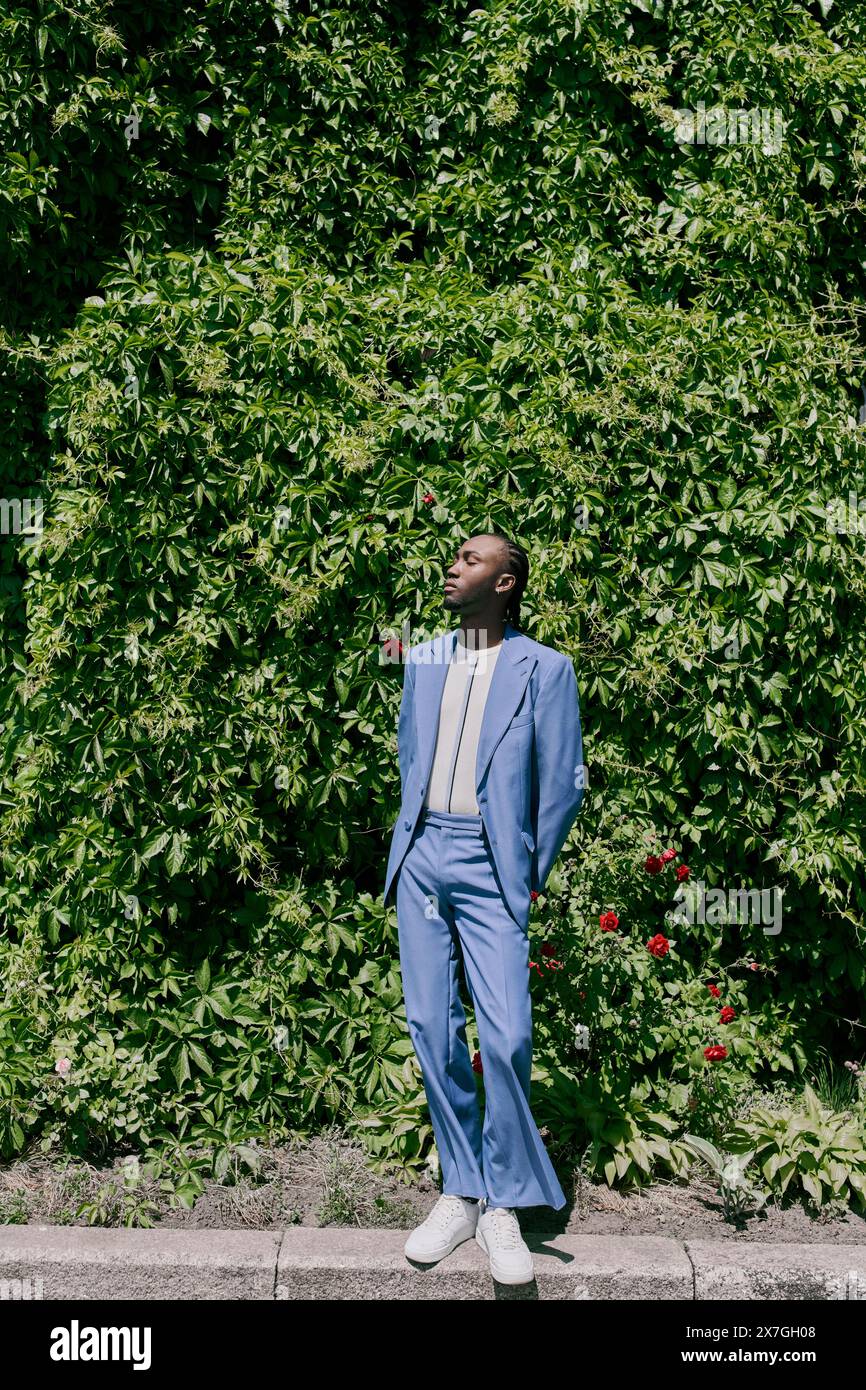 A stylish man in a blue suit stands confidently on a city sidewalk ...