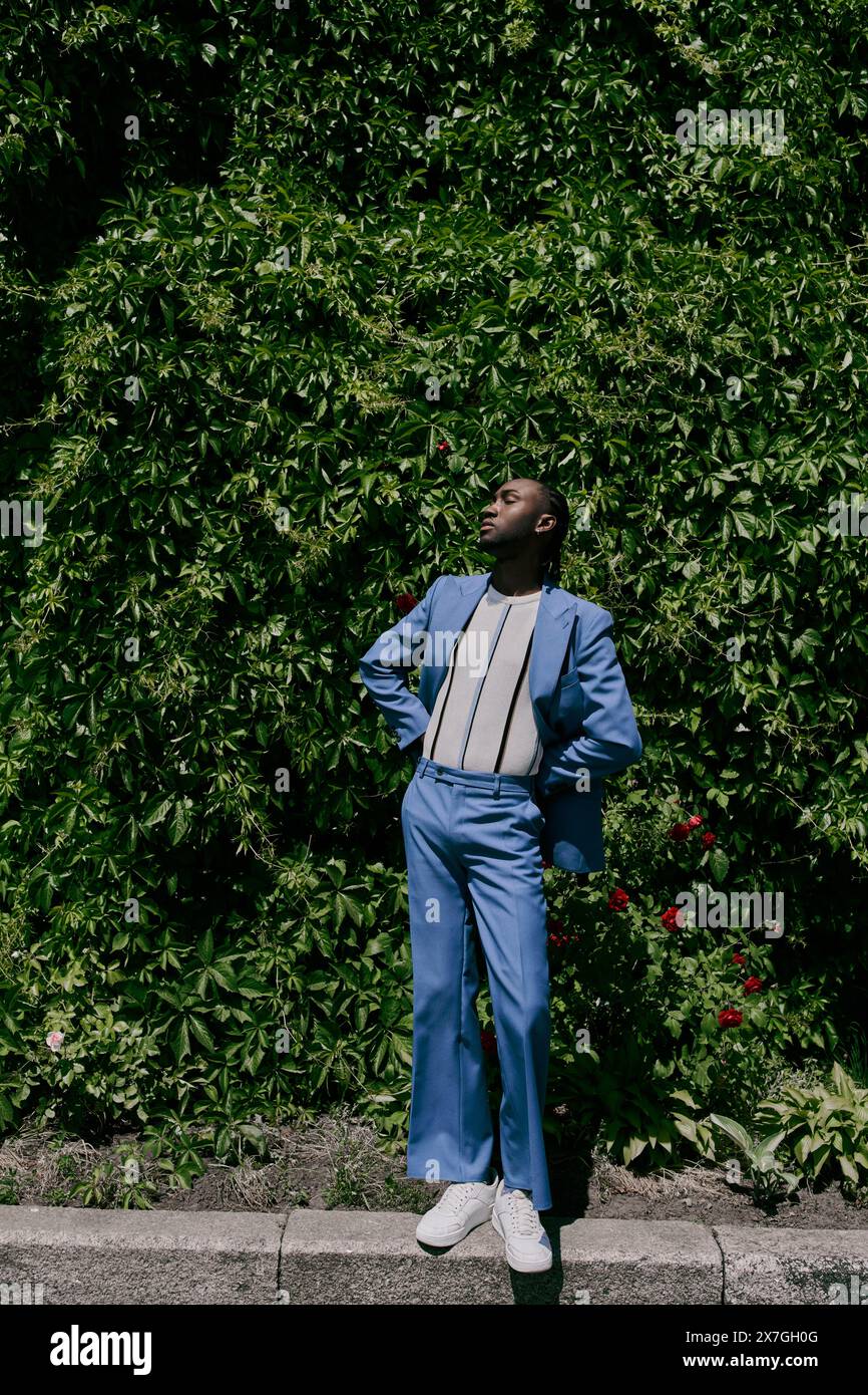 A stylish man in a blue suit stands confidently on a urban sidewalk ...
