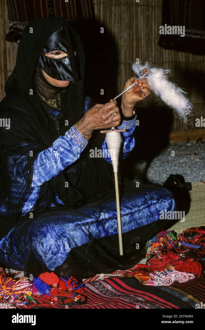 Muscat, Oman, Arabian Peninsula, Middle East - Bedouin woman spinning wool.  She wears a black abaya, and a face mask called a birqa. Stock Photo