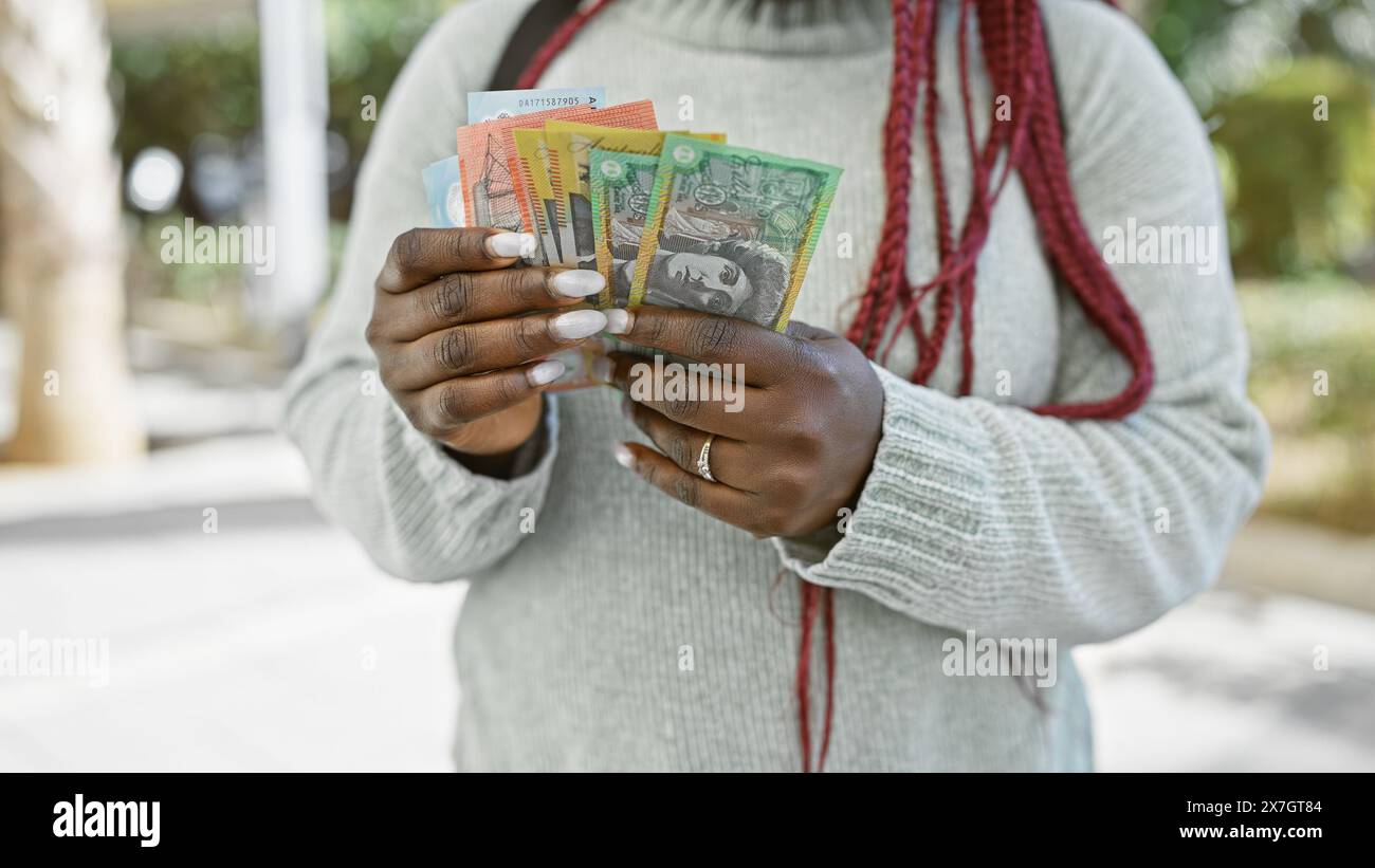 Australian currency held by a woman with braids outdoors in a lush park ...