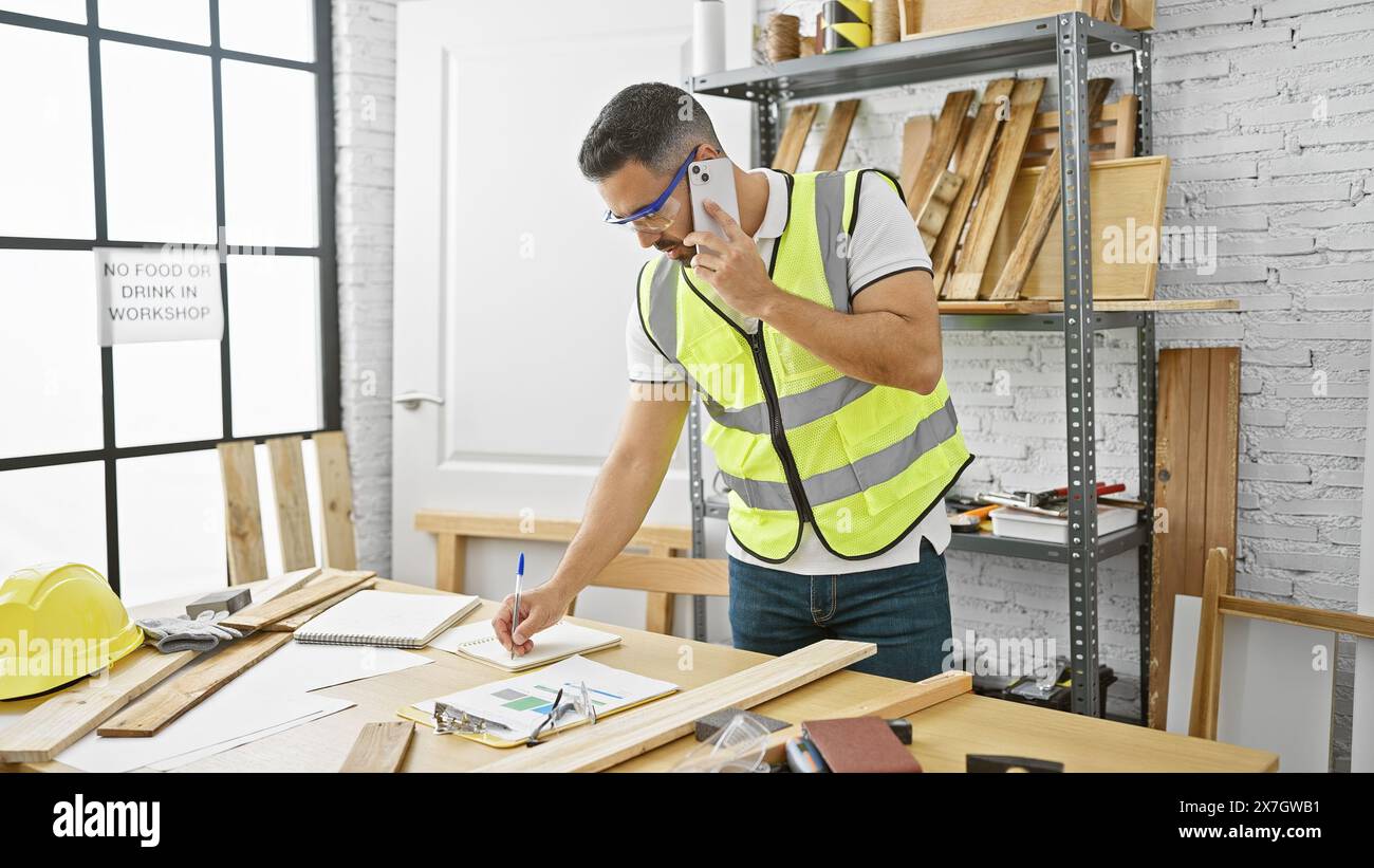 Handsome hispanic man using phone while working in a bright carpentry workshop Stock Photo