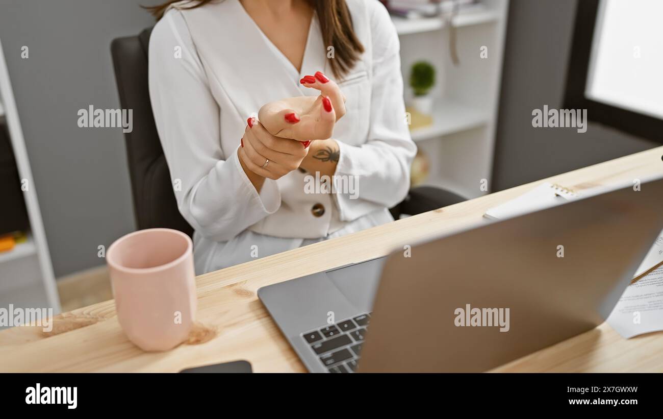 A young woman experiences wrist pain while holding a piggy bank in an office setting. Stock Photo