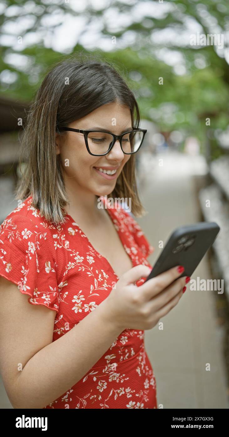 Cheerful beautiful hispanic woman in glasses happily using smartphone ...