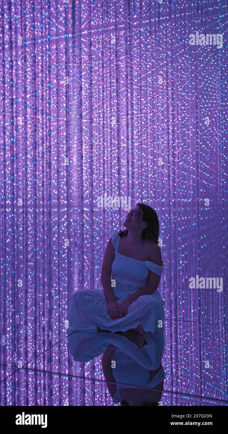 Smiling beautiful hispanic woman experiencing immersive futuristic exhibit at modern museum - lasers, lights, innovation at their best! Stock Photo