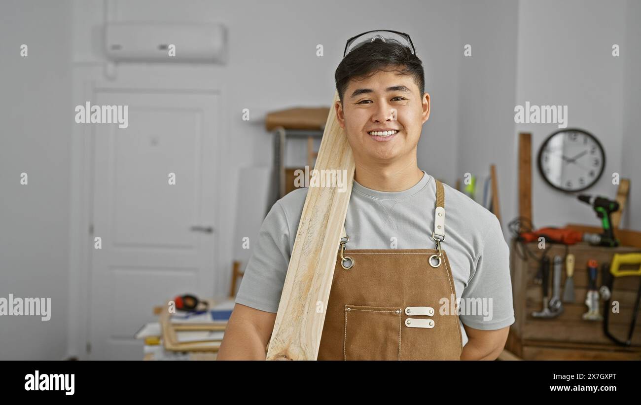 Smiling asian man holding wood in a wellequipped carpentry studio