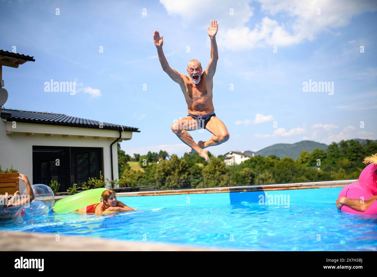 Group of cheerful seniors shaving fun in pool jumping, swiming and ...