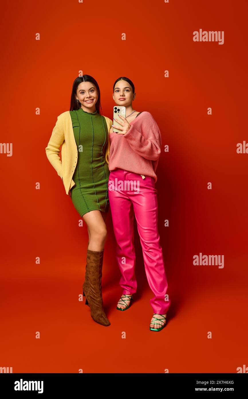 Two pretty teenage brunettes in casual attire stand together in front of a vibrant red background. Stock Photo