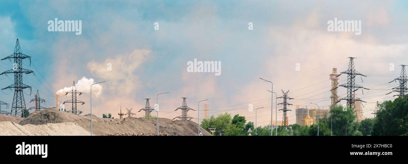A wide panoramic view of an industrial landscape featuring power lines and smoke stacks emitting pollutants. Ideal for website headers and articles, highlighting industrial impact on the environment Stock Photo