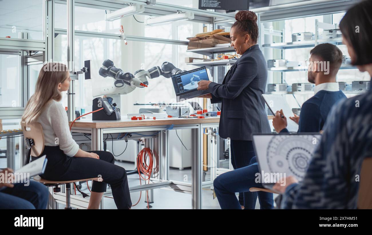 Enthusiastic Black Female Chief Engineer Explains to Computer Scientists and Developers Principles of Robotic Arm Controls. Young Intelligent People Acquire New Technical Information. Stock Photo