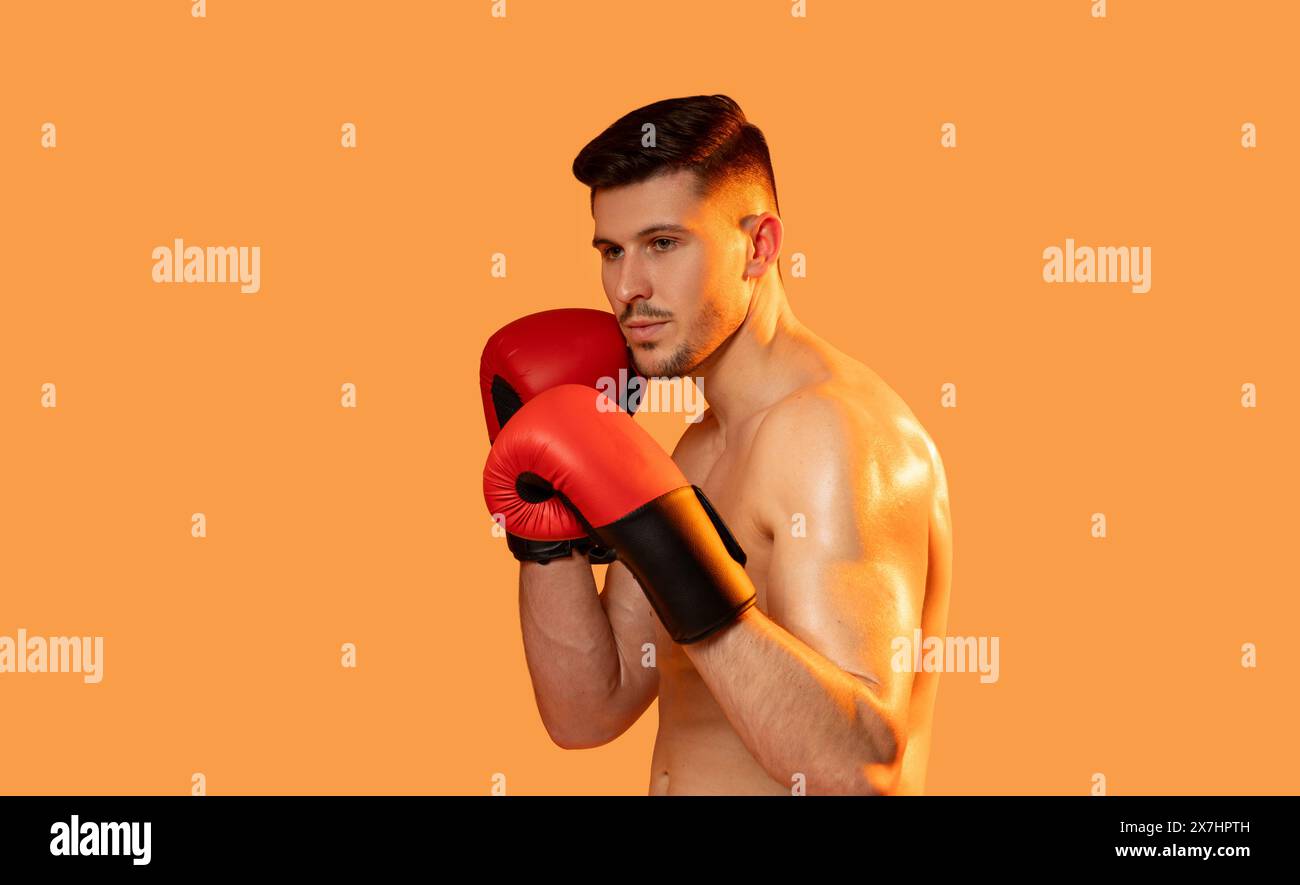 Man in Boxing Gloves Poses on Orange Background Stock Photo