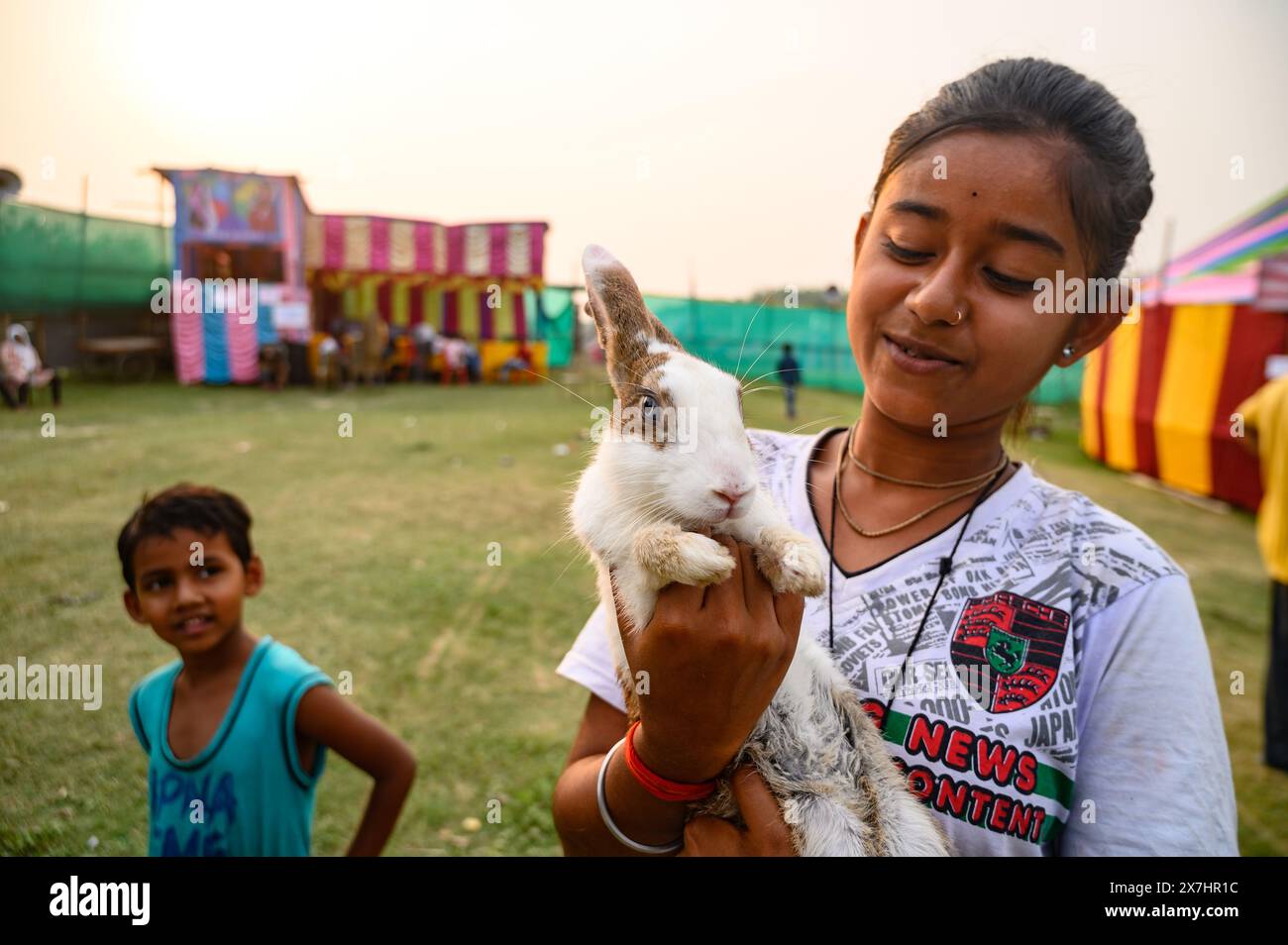 A young village girl and her brother visit the fair with their pet rabbit. The rabbit is repeatedly trying to escape and giving different expressions. A recent study found that domestic rabbits have smaller brains relative to their body size compared to their wild counterparts. Rabbits can carry zoonotic diseases, which can be transmitted to humans through bites and scratches, Pasteurellosis, Tularemia also known as 'rabbit fever' or 'deer fly fever'. Natipota, West Bengal. India. Stock Photo