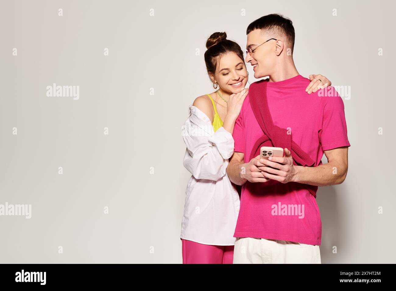 A stylish young man and woman standing close together in a studio, expressing love and connection against a grey background. Stock Photo