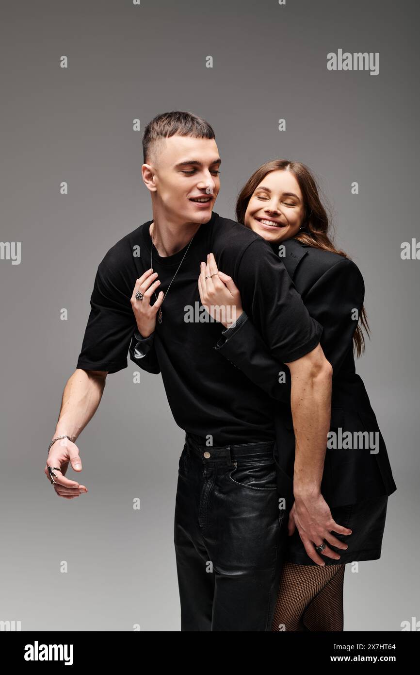 A young man and woman strike a pose together in a studio with a grey ...