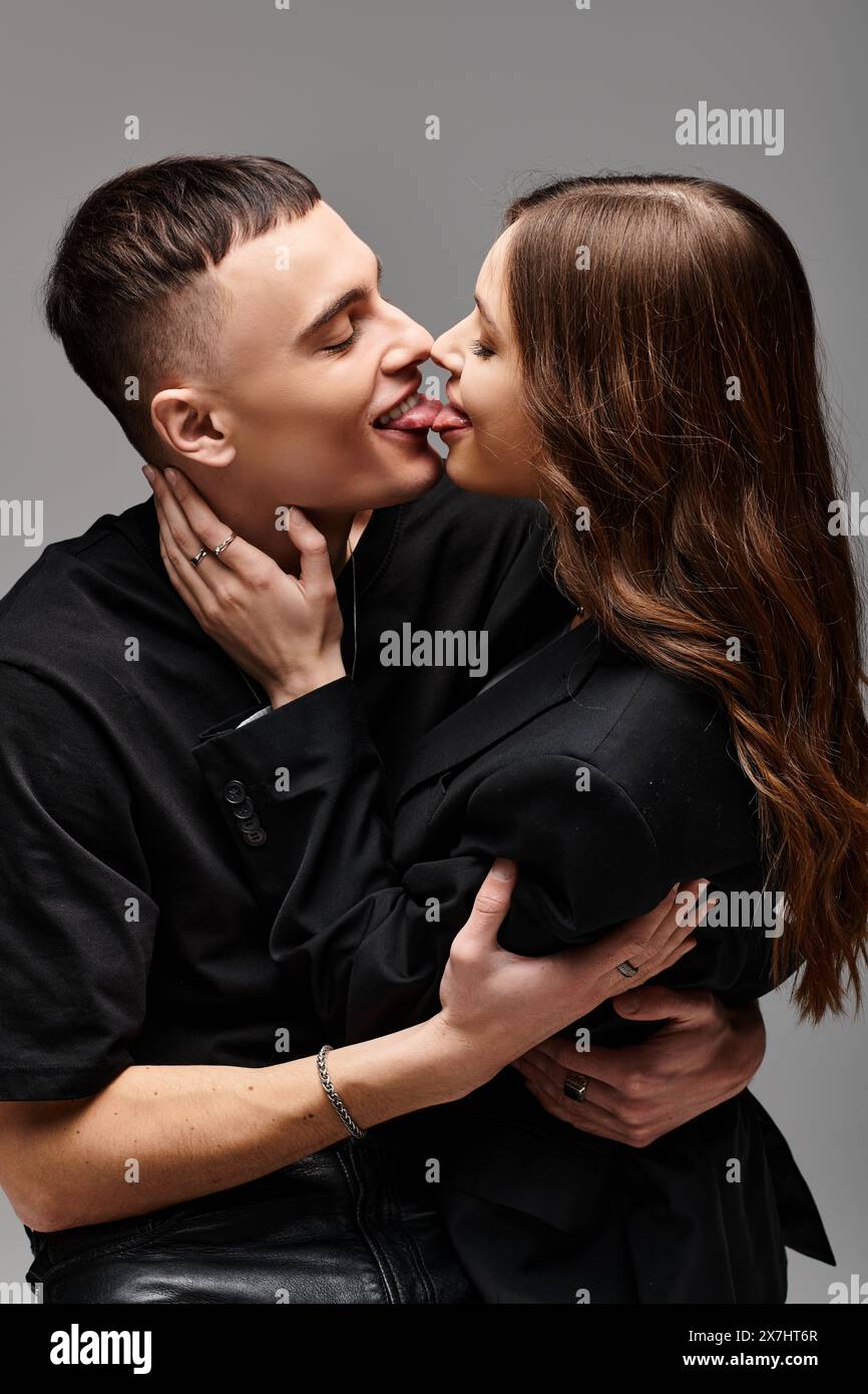 A young man and woman lock lips in a passionate kiss against a grey ...