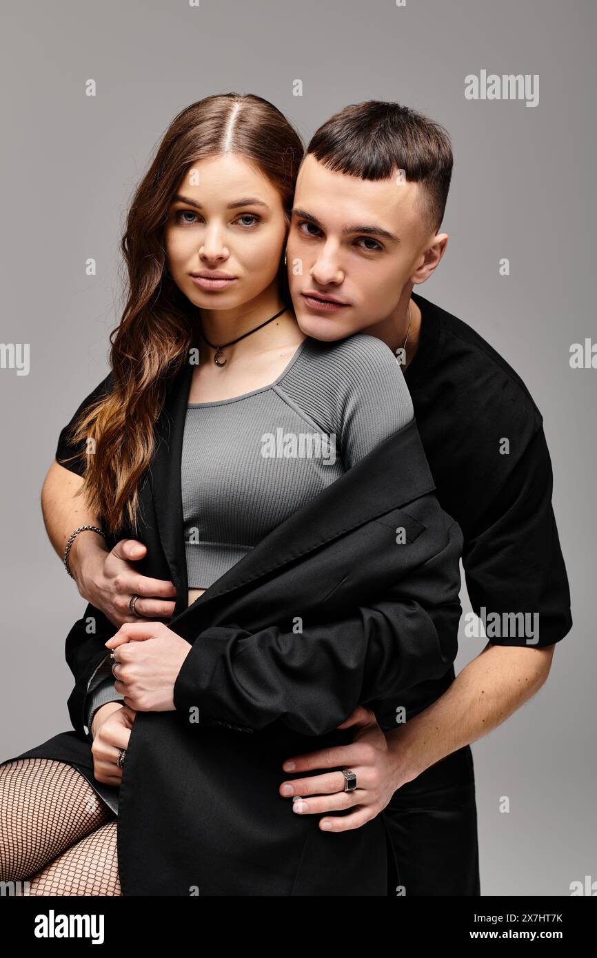 A young man and woman strike a pose together in a studio with a grey ...