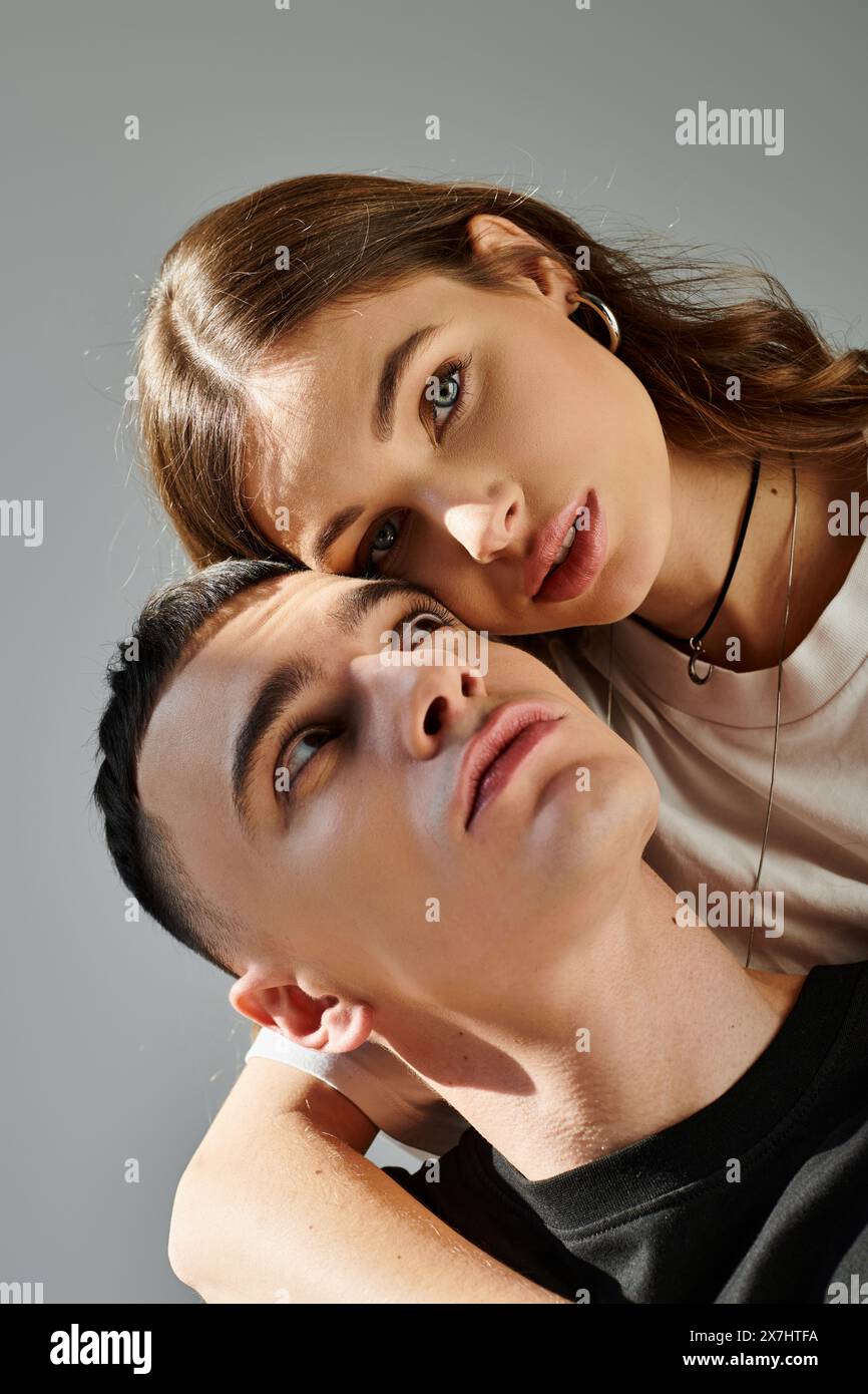 A young man and woman pose together in a studio against a grey ...