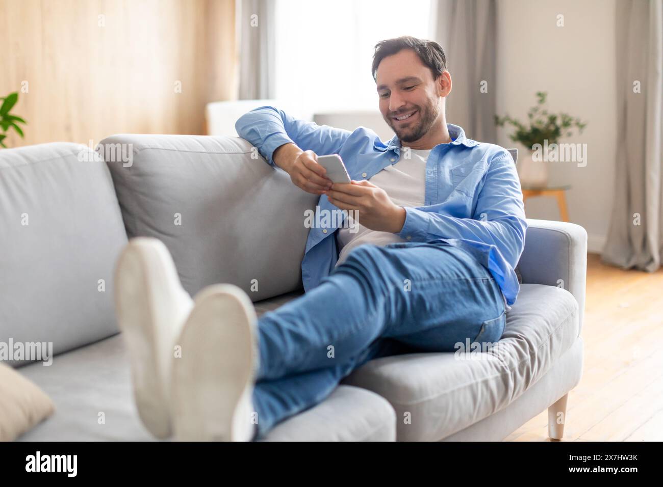Happy Man Reclining on Couch Using Phone Stock Photo