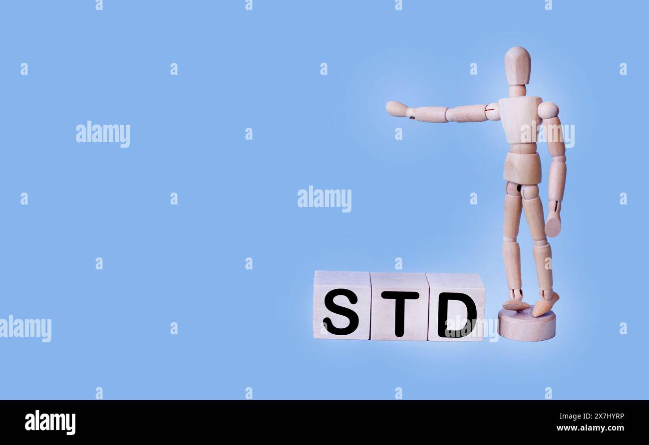 A wooden block forms the word STD on a blue background, with a wooden doll nearby. Healthcare concept.. Stock Photo