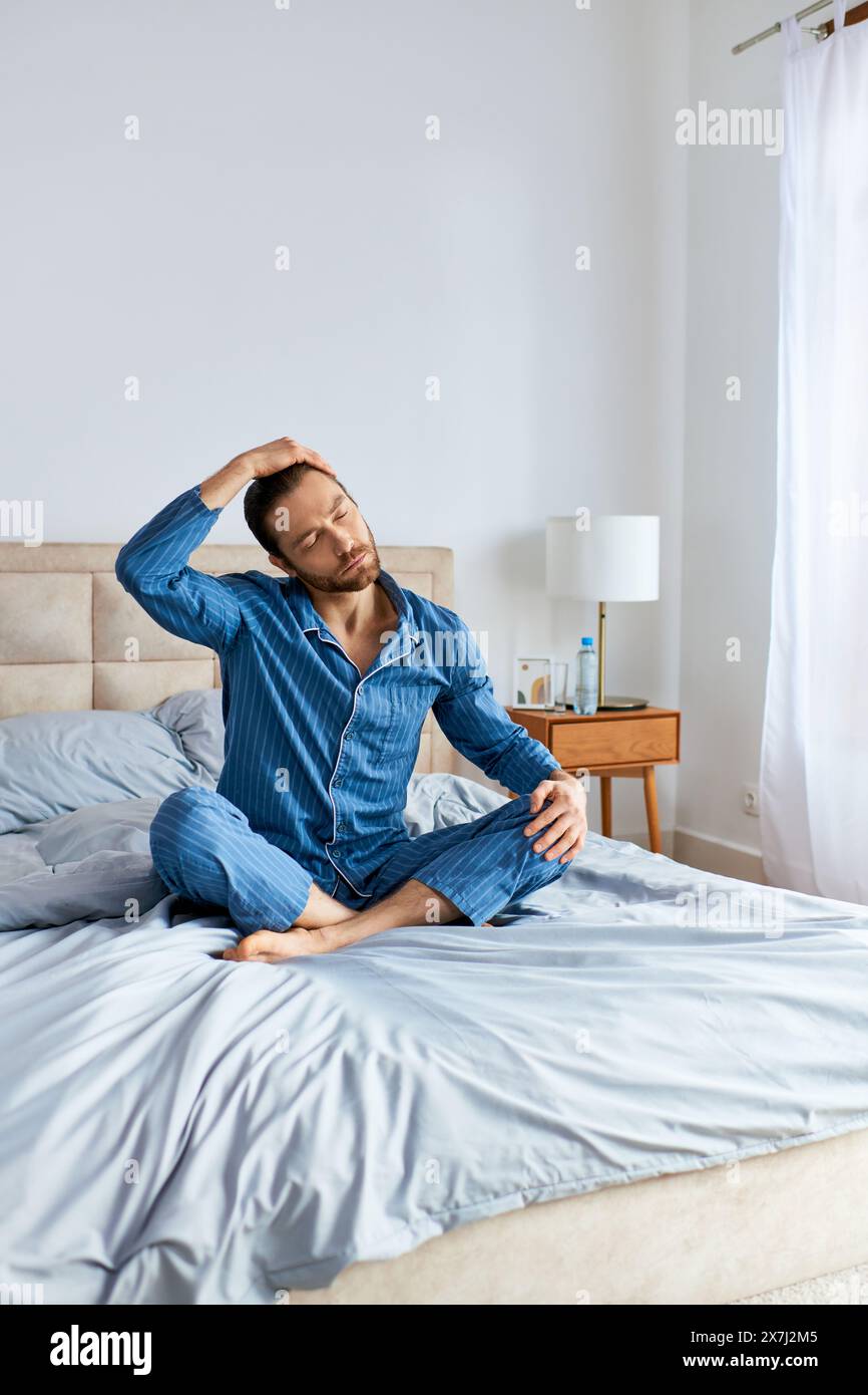 A man in pajamas sits calmly on top of a bed, practicing yoga poses. Stock Photo