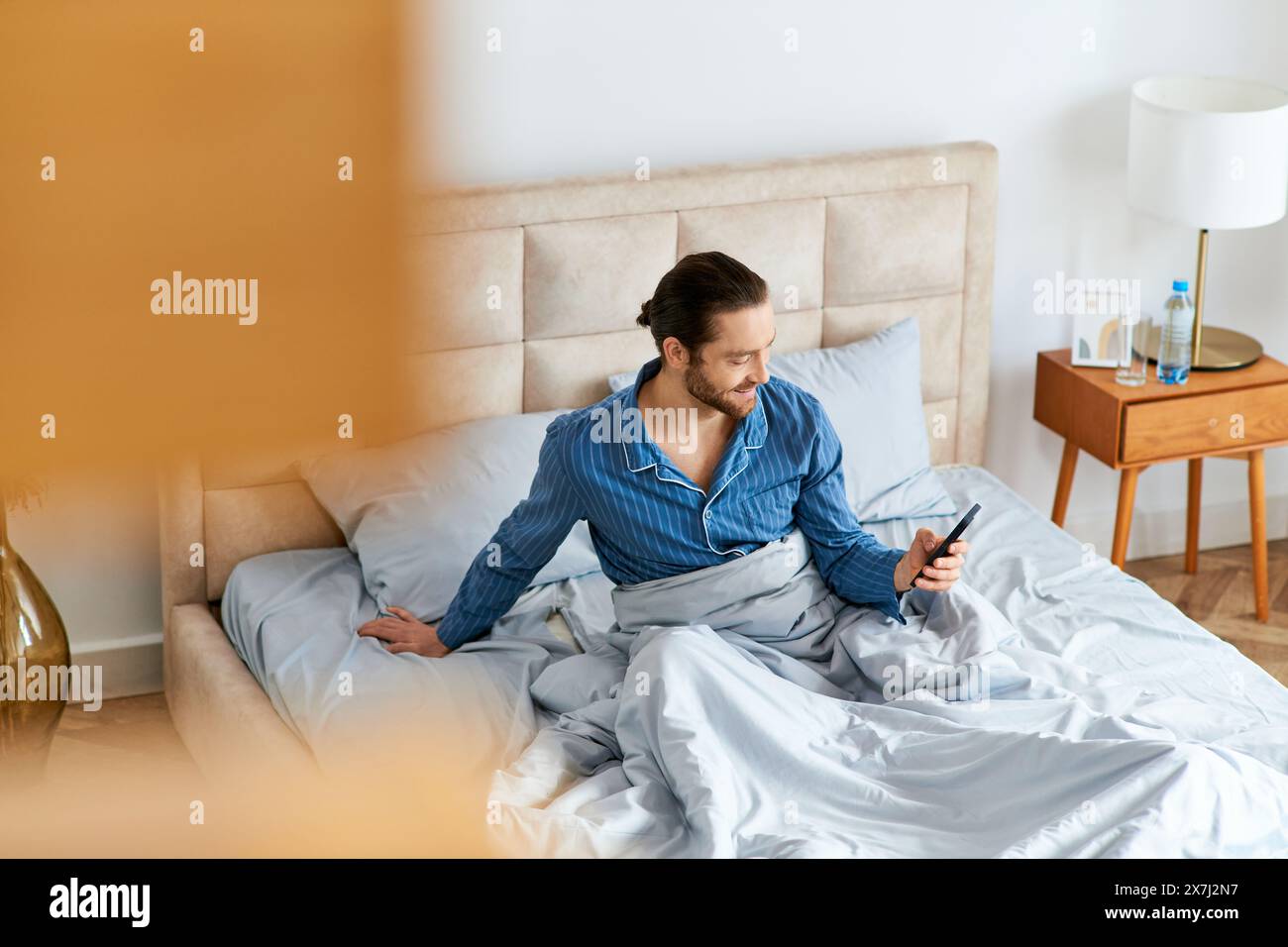 A man sits on his bed, engrossed in his cell phone screen. Stock Photo
